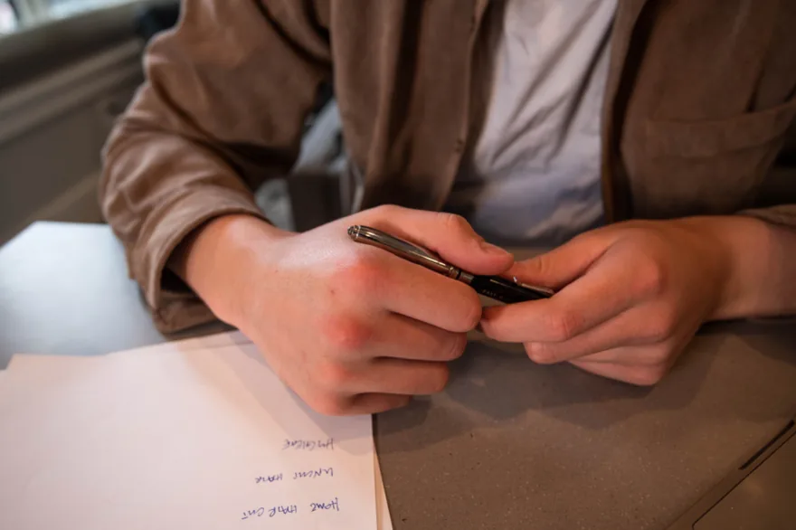Manos de una persona sujetando un boligrafo sobre un documento manuscrito en una mesa de reuniones